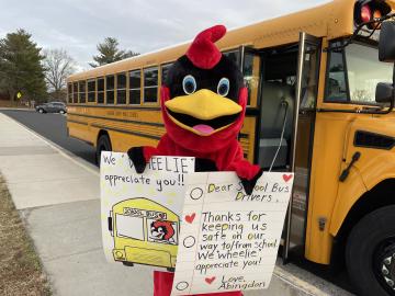 Abingdon Cardinal standing in front of school buses with posters showing appreciation for the bus drivers